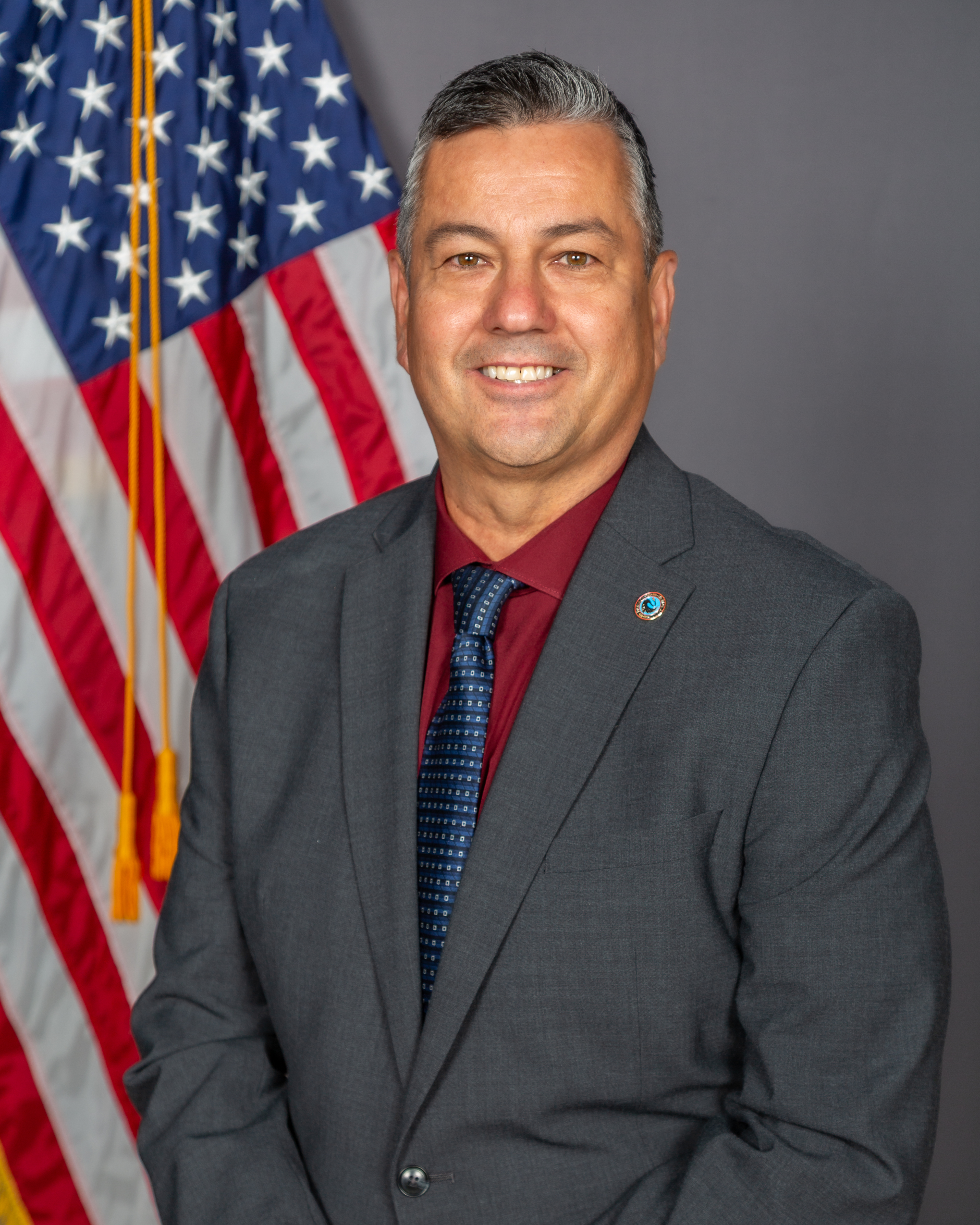 Acting Assistant Sheriff Greg Harrera, in a suit, poses in front of the American Flag